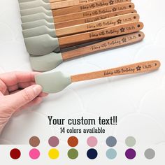 a hand holding a wooden spatula with custom text on it and color swatches