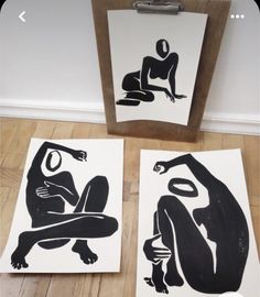 three black and white paintings sitting on top of a wooden floor