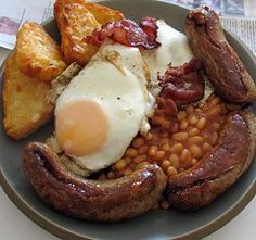 an english breakfast with eggs, beans and sausage on a plate in front of a newspaper