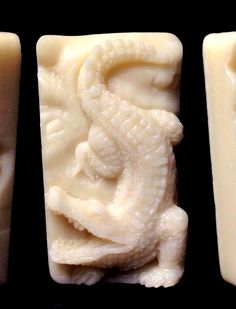 three soaps with carved dragon designs on them, one in white and the other in yellow