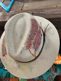 a white hat with colorful feathers on it sitting on top of a wooden table next to other items