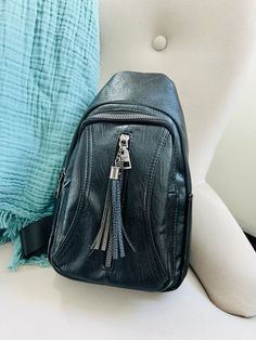 a black leather backpack sitting on top of a white chair next to a blue pillow