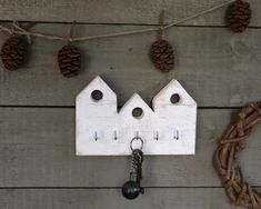 a white house shaped key holder hanging from a string with pine cones on the background