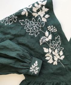 a green dress with white flowers and leaves on the front, sitting on top of a table