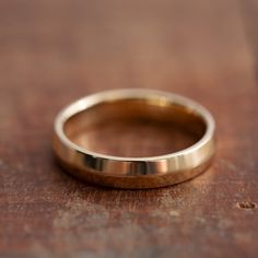 a gold wedding ring sitting on top of a wooden table next to a brown surface