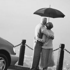 an older couple embracing under an umbrella on the top of a hill in black and white