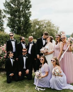 a group of people standing next to each other in front of bushes and flowers on the grass