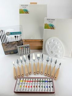 an assortment of paint brushes and other art supplies in front of a white board with pictures on it