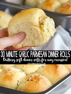 a hand holding a piece of garlic parmesan dinner rolls over a pan of other rolls