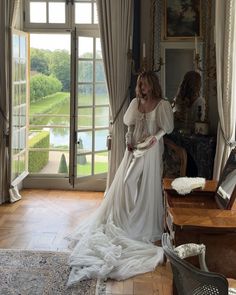 a woman standing in front of a window wearing a white dress