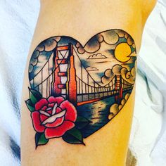 a tattoo on the leg of a woman with a rose and bridge in the background