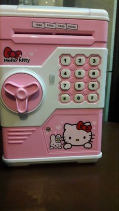 a pink hello kitty toy machine sitting on top of a wooden table next to a wall