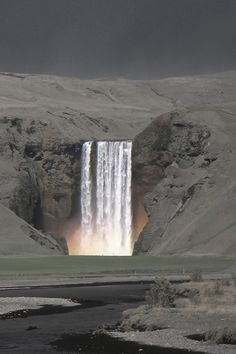 a large waterfall in the middle of a mountain range with rainbow colored water coming from it