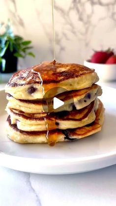 a stack of pancakes with syrup being drizzled over them on a white plate