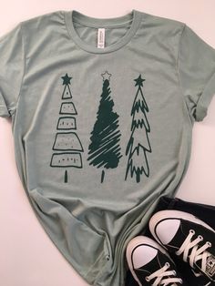 Christmas Shirt. Womens Christmas Shirt. Christmas Tree Tee. Christmas T-Shirt. Christmas Tees. Holiday Shirts. Christmas Graphic Tee. Everyone needs a favorite tee. This tee can be just that. This one has a cute tree design on a heather dusty blue colored tee with a dark green ink. It's soft, comfortable, and stylish. Grab one for yourself or your friend who loves Christmas! Christmas Tree Tee Bella/Canvas brand Unisex Fitted Tee, 4.2 oz 100% Combed and ringspun cotton The tee is heather dusty Christmas Green Cotton Tops, Green Cotton Christmas Tops, Festive Green Casual Tops, Relaxed Fit Short Sleeve T-shirt For Holiday, Green Cotton Holiday Top, Green Cotton Top For Holidays, Festive Green Short Sleeve Top, Casual Green Holiday Tops, Casual Green Top For Holiday