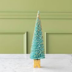 a small blue christmas tree sitting on top of a white marble counter next to a green wall