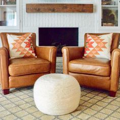 two brown leather chairs sitting in front of a fire place with pillows on the back