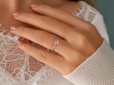 a woman's hand with a diamond ring on her left hand, wearing a white lace top