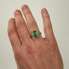 This ring lives at Danielle Shop in San Francisco. Please contact Hilary to inquire about this piece. You won't be able to take your eyes off of this radiant cut green tourmaline ring. Aptly named, this stone radiates an array vibrant green hues. The double band compliments the crossbar and provides a luxurious contrast to the stone's geometric and longitudinal facets. A true one of a kind. 18k gold. 2.42 carat radiant cut green tourmaline. Size 7. Emerald Cut Tourmaline Ring Fine Jewelry, Emerald Cut Tourmaline Ring In Fine Jewelry Style, Emerald Cut Tourmaline Gemstone Rings, Modern Green Emerald-cut Jewelry, Green Tourmaline Ring For May Birthstone, Emerald Cut Tourmaline Ring For Anniversary, Green Emerald Cut Ring With Bezel Setting, Modern Emerald Rings With Baguette Cut, Modern Emerald Cut Emerald Ring