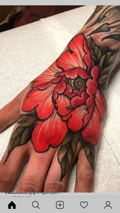 a person's hand with red flowers on it and green leaves in the middle