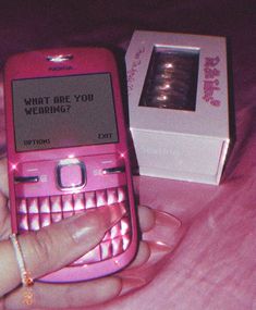 a person holding a pink cell phone in their hand next to a box with the message what are you wearing?