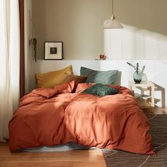 a bed with an orange comforter in a bedroom next to a window and wooden floor