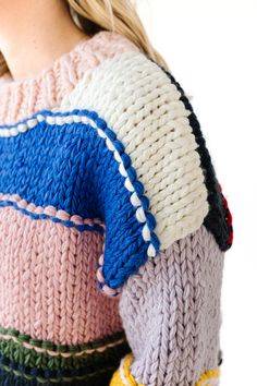 This sweater is a striking example of a chunky, hand-knit garment featuring a patchwork-like design with bold, contrasting colors. The sweater is made from thick yarns, creating a warm and cozy feel that is ideal for colder weather. It has a high, slightly ribbed neckline, which adds to the snug, comfortable look of the piece.

The design is characterized by wide, horizontal stripes in a variety of colors, including pastel pink, deep blue, lavender, mustard yellow, forest green, and bold red.