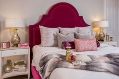 a bed with pink headboard and pillows on top of it next to two lamps