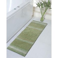 a green rug is on the floor next to a white bathtub and plant in a vase