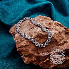 a silver chain bracelet sitting on top of a piece of wood next to a rock