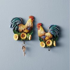 two roosters are hanging on the wall with keys in their mouth and sunflowers around them