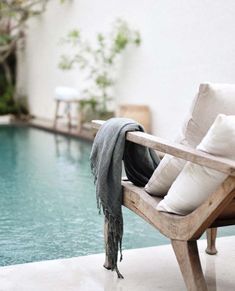 a wooden chair sitting next to a swimming pool with pillows on it's back