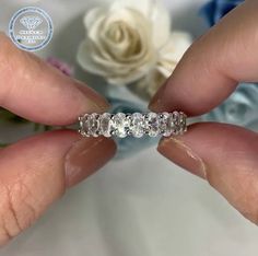 a woman's hand holding a wedding ring with three stones on it and flowers in the background