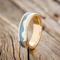 a wedding ring with blue and white marble inlays on it sitting on a wooden surface