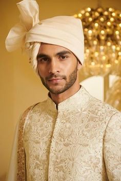 a man wearing a white turban standing in front of a wall with lights