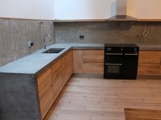 an empty kitchen with wooden floors and black stove top oven in the center, surrounded by concrete counter tops