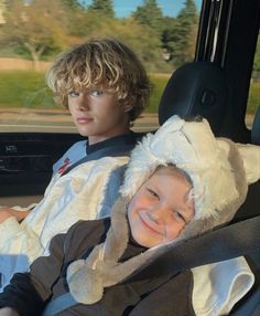 two young boys sitting in the back seat of a car, one wearing a sheep hat