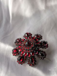 “The garnet is a red gem, but not like the ruby; its red is much more like that of a flame … It forms far in the east … If correctly cut and polished, it will reveal all its beauty and perfection.” – Aristotle, ca. 322 B.C. Hailing from the hills of what we now call the Czech Republic, these intricately cut garnet jewels from Bohemia were wildly popular in the 1890’s and throughout the Victorian era. Typically set in 6ct Garnet Gold, such as this example, bohemian garnet jewels came at a price most could afford. For the price of one large gold jewel, you could for example, buy 3 bohemian garnet pieces; this is perhaps why so many exquisite examples survive today, people were dripped out the Bohemian Garnet! This sizable floral brooch from the end of the 19th c is truly a knockout, and a be Antique Red Brooch Jewelry, Antique Red Brooch, Ornate Red Jewelry Brooch, Antique Red Brooch For Formal Occasions, Elegant Red Brooches Collectible, Antique Red Wedding Brooch, Victorian Jeweled Formal Brooches, Antique Red Brooch As Gift, Formal Ruby Brooch Jewelry