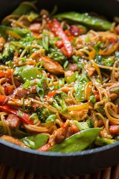 a pan filled with noodles and vegetables on top of a wooden table