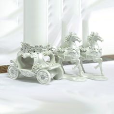 three white candles sitting on top of a table next to a horse and carriage figurine