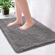 a person standing on top of a gray rug next to a potted green plant