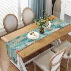 a wooden table topped with a white plate and vase filled with flowers next to two chairs