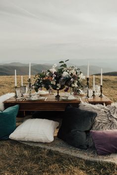 a table with candles and flowers on it in the middle of an open field surrounded by pillows