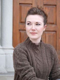 a woman sitting in front of a wooden door with her hand on the handlebars