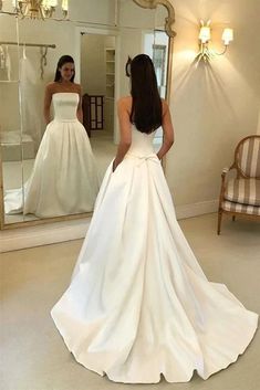 a woman standing in front of a mirror wearing a white wedding dress and looking at herself in the mirror