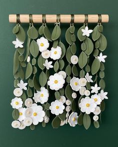 paper flowers and leaves are hanging on a green wall with a wooden stick in the foreground