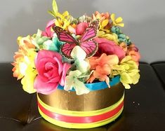 a colorful flower arrangement in a gold and blue container on top of a black table