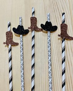 three straws decorated with cowboy hats and sparkle sticks on top of a wooden table