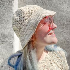 a woman wearing glasses and a knitted hat smiles at the camera while standing in front of a wall