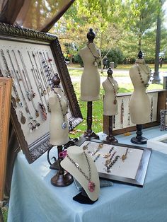 several mannequins and jewelry displayed on a blue tablecloth in front of an old frame